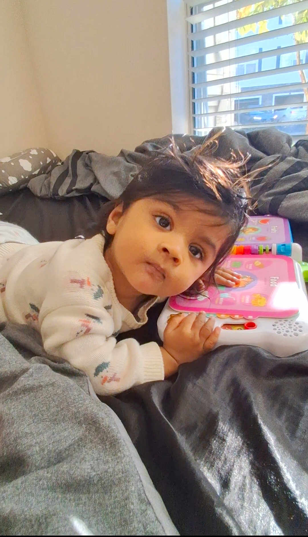 Easan is registered to the contest to win money with this photo: baby, bed, blanket, child, clothing, curious, educational_toy, expression, face, hand, head, indoor, lying_down, person, playing, room, sleeve, sunlight, toy, window