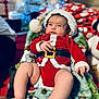 baby, infant, christmas, holiday, santa_outfit, blanket, present, gift, decorations, indoors, cute, festive, child, smiling, person, red_clothing, white_trim, holiday_season, cozy, celebration