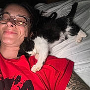 Chester joined the competition — help win amazing prizes! person, glasses, smile, kitten, cat, sleeping, bed, pillow, red_shirt, tattoo, indoor, closeup, resting, cute, pet, animal, human, comfort, relaxation, affection
