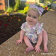 Amelia is registered to the contest to win money with this photo: baby, child, infant, sitting, outdoors, sidewalk, garden, flowers, floral_outfit, headband, bow, smiling, face, portrait, suburban, house, sunlight, pavement, social_media_watermark, happy