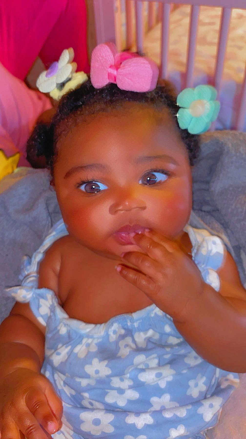 Jalinah Miller is registered to the contest to win money with this photo: baby, child, infant, face, hand, dress, flower_pattern, hair_accessories, pink_bow, blue_flower, curly_hair, skin, cute, portrait, indoor, fingers_in_mouth, expression, seated, closeup, adorable