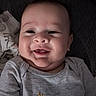 baby, blanket, child, chubby_cheeks, close_up, cute, face, giraffe, gray_clothing, happy, head, indoors, infant, lying_down, onesie, patterned_cloth, person, portrait, smiling, soft_toys