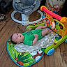 Alexander is registered to the contest to win money with this photo: baby, infant, green_onesie, play_mat, toy_arch, blanket, wooden_floor, baby_rocker, floor, indoor, child, person, face, head, limbs, colorful, comfort, relaxing, cute, home
