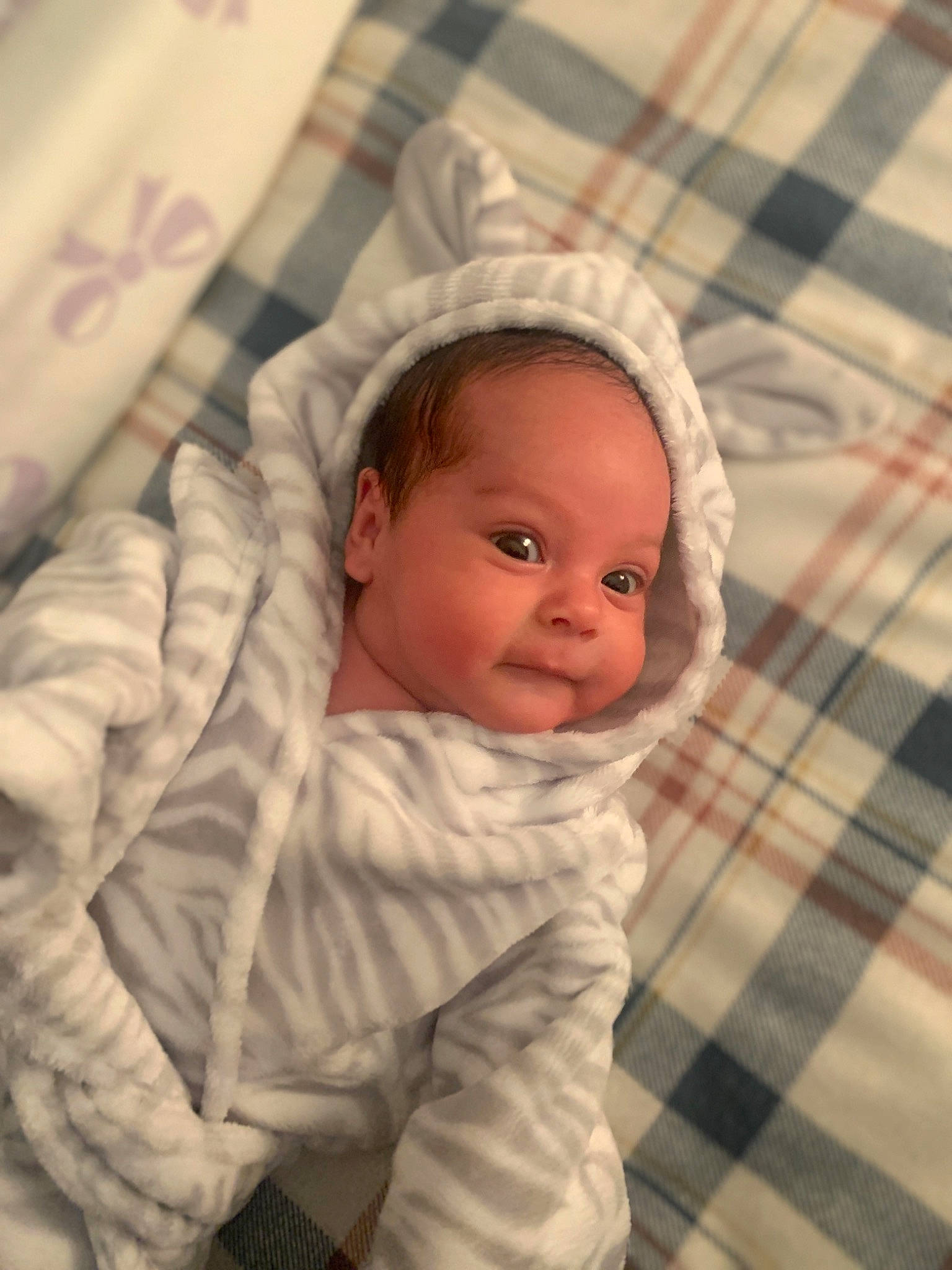 Liana is registered to the contest to win money with this photo: baby, baby_toddler_clothing, cheek, child, chin, comfort, eyebrow, facial_expression, flooring, iris, linens, nose, pattern, person, plaid, skin, sleeve, smile, tartan, textile