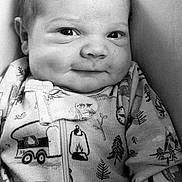 Colton is registered to the contest to win money with this photo: baby, infant, smile, face, onesie, clothing, pattern, black_and_white, portrait, cute, child, young, cozy, indoors, person, newborn, expression, sitting, soft, closeup