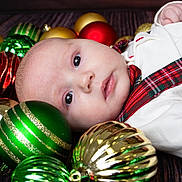 Liam joined the competition — help win amazing prizes! baby, infant, christmas_ornaments, holiday, festive, red, green, gold, face, portrait, cute, decorations, holiday_clothing, tartan, plaid, white_clothing, lying_down, closeup, indoors, celebration