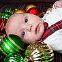 baby, infant, christmas_ornaments, holiday, festive, red, green, gold, face, portrait, cute, decorations, holiday_clothing, tartan, plaid, white_clothing, lying_down, closeup, indoors, celebration