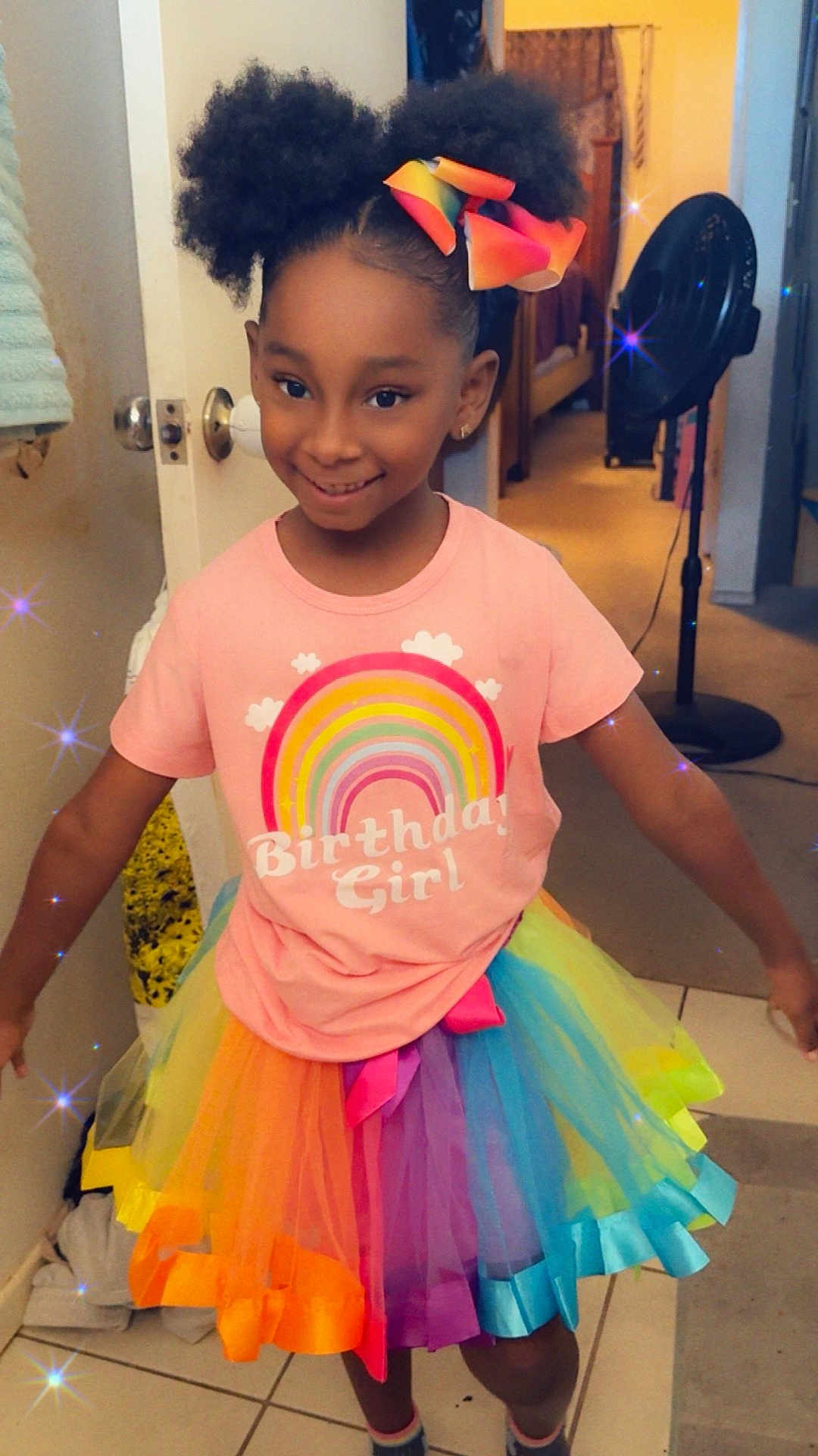 Summer is registered to the contest to win money with this photo: child, birthday_girl, rainbow, tutu, hair_bow, smiling, indoor, fan, door, tile_floor, colorful_clothing, happy, person, sparkles, celebration, girl, cute, fashion, home, portrait