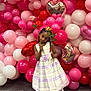 child, girl, balloon, flower, dress, white_dress, purple_stripes, pink_balloon, red_balloon, heart_shaped_balloon, carpet, indoor, playful, portrait, standing, holding_flowers, braided_hair, black_shoes, white_tights, celebration