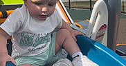 Kasen is registered to the contest to win money with this photo: toddler, child, slide, playground, outdoor, daylight, white_shoes, shorts, tshirt, blonde_hair, plastic_slide, fence, park, sunny, recreation, casual_clothing, young_child, sitting, play, fun