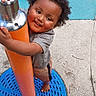 barefoot, blue_surface, child, clothing, concrete, curly_hair, fun, gray_surface, happy, holding, metal, orange, outdoor, person, play, playground, pole, smiling, toddler, young_child