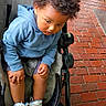 Zyair is registered to the contest to win money with this photo: baby, blue_hoodie, brick_pavement, casual_clothing, child, curly_hair, daylight, expression, footwear, hands, legs, outdoor, person, seat, sidewalk, sneakers, stroller, toddler, urban, young_child
