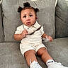 Prince is registered to the contest to win money with this photo: toddler, child, sitting, couch, gray_couch, pigtails, curly_hair, white_sneakers, socks, sunglasses, plastic_wrapper, cream_outfit, indoor, portrait, looking_up, expression, cute, fashionable, young_child, person