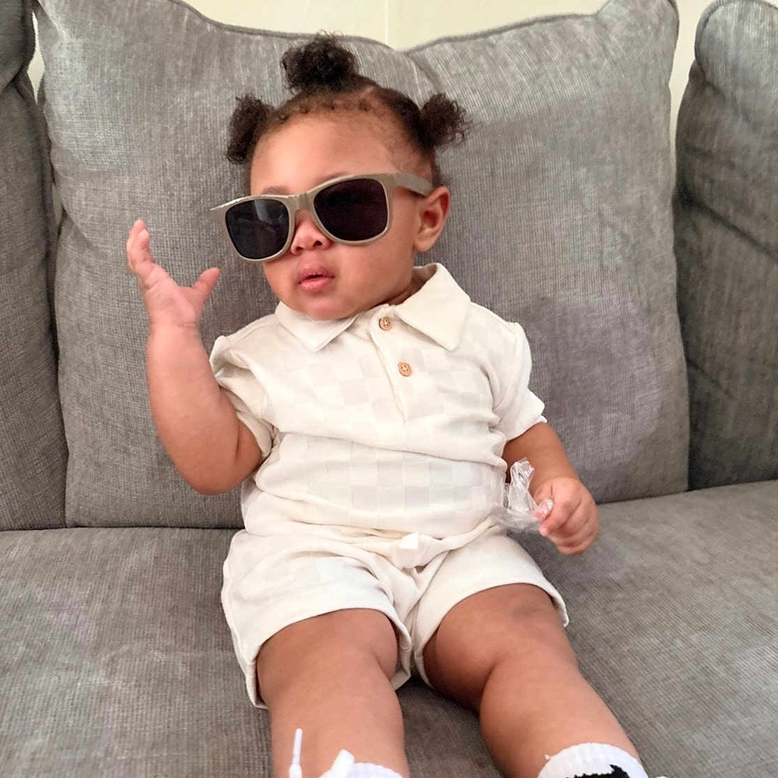 Prince is registered to the contest to win money with this photo: toddler, child, sunglasses, white_shoes, socks, couch, gray_couch, shorts, polo_shirt, hairstyle, indoor, cute, fashion, casual, person, young_child, sitting, relaxed, accessory, footwear