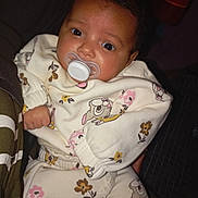 Kaylis a rejoint le concours — aidez-le/la à gagner de superbes lots ! baby, infant, pacifier, onesie, floral_print, big_eyes, close_up, portrait, indoor, dark_hair, brown_skin, hand, sitting, cozy, bedtime, cute_expression, sleepwear, blanket, soft_light, pattern_clothing