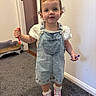 Wren is registered to the contest to win money with this photo: toddler, child, indoor, denim_overalls, white_shirt, pink_sneakers, curly_hair, markers, carpet, pet_bed, doorway, playful, cute, smiling, person, feet, socks, standing, home, young_child