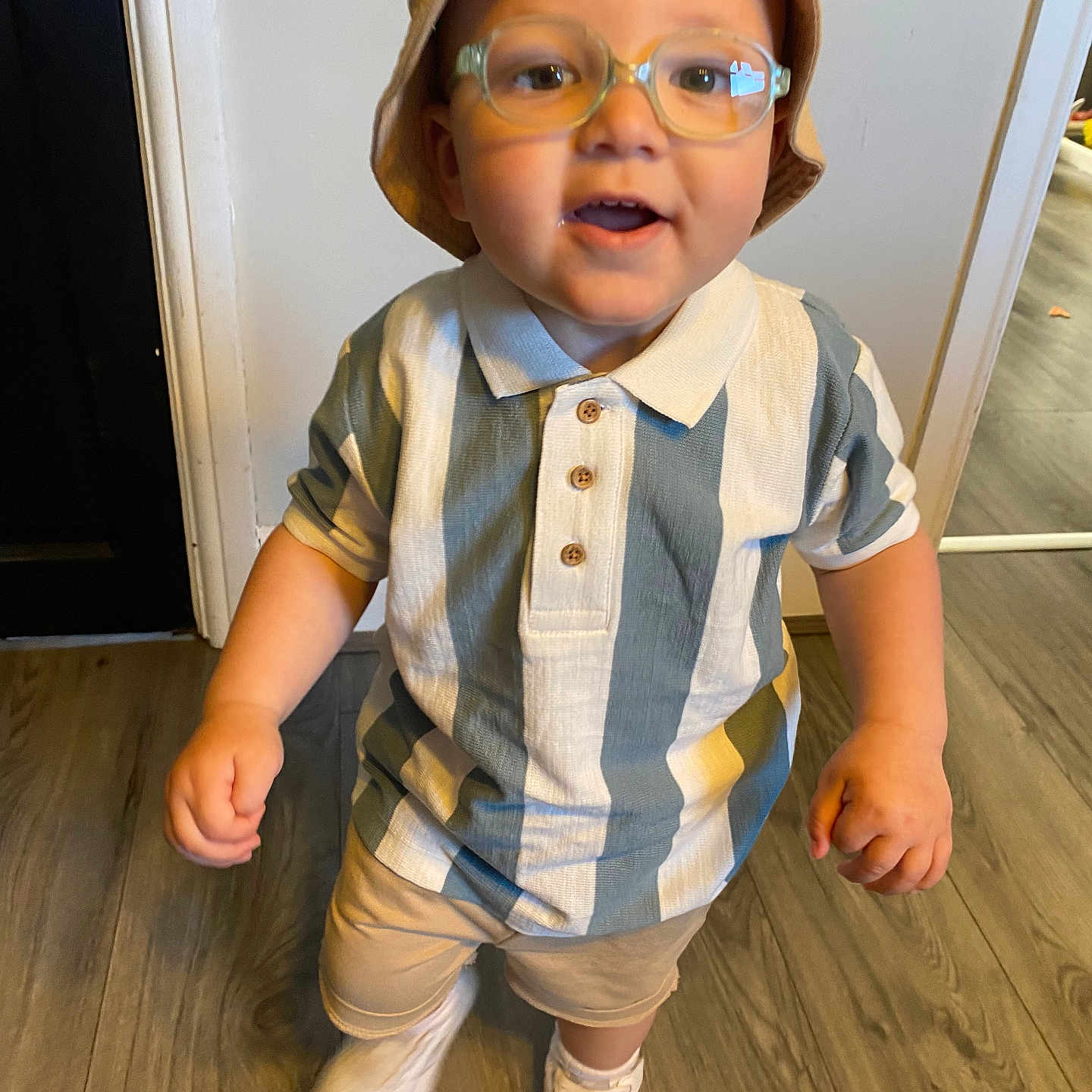 Arlo-Jay is registered to the contest to win money with this photo: bucket_hat, child, cute, fashion, floor, glasses, happy, hat, indoor, person, portrait, shirt, shorts, smiling, striped_shirt, toddler, walking, white_sneakers, wooden_floor, young_child