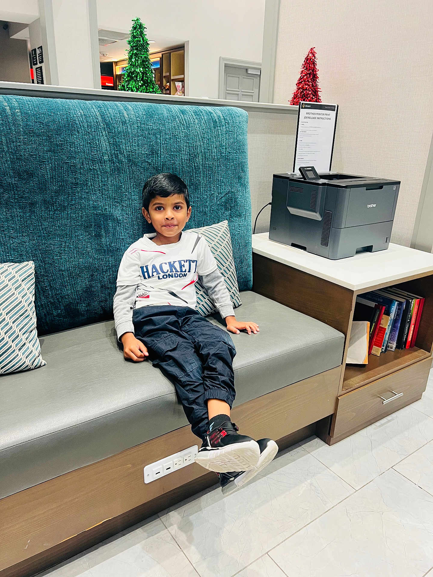 Thejus joined the competition — help win amazing prizes! child, boy, sitting, bench, cushion, printer, books, indoor, casual_clothing, holiday_decorations, tinsel, floor_tiles, modern_furniture, curious_expression, black_pants, white_shirt, sneakers, side_table, room, portrait