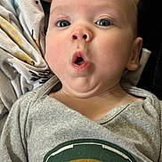 Michael is registered to the contest to win money with this photo: baby, blanket, cartoon_print, child, clothing, cute, expression, eyes, face, head, human, indoors, infant, mouth, onesie, portrait, skin, soft, surprised, tongue