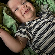 Michael is registered to the contest to win money with this photo: baby, child, smile, striped_shirt, blanket, green_blanket, pacifier, infant, lying_down, happy, cheeky, soft_texture, closeup, face, arm, clothing, person, comfortable, indoors, cute