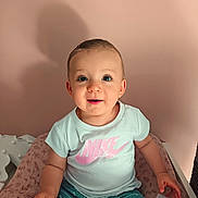 Victoria a rejoint le concours — aidez-le/la à gagner de superbes lots ! casual_clothing, child, cushion, cute, face, hair_clip, hand, happy, indoor, nike_logo, patterned, person, pink_wall, seat, shadow, shorts, sitting, smile, toddler, tshirt