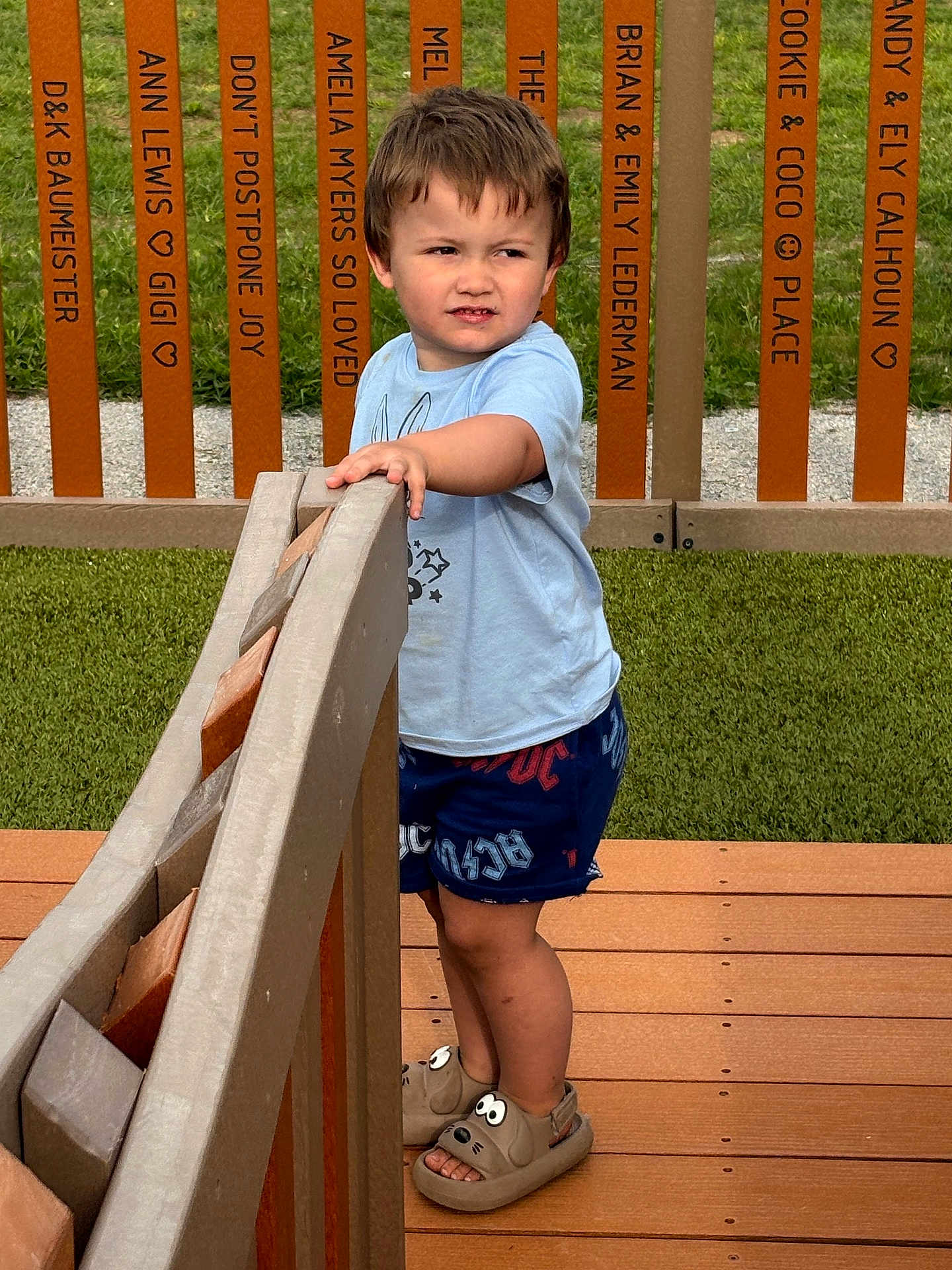 Uhtred joined the competition — help win amazing prizes! child, boy, standing, wooden_deck, railing, fence, grass, outdoor, shorts, shirt, sandals, expression, curious, playful, footwear, summer, daytime, names, messages, background