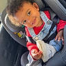 Qassim participe au concours pour gagner de l'argent avec cette photo : car_interior, car_seat, casual_clothing, child, curly_hair, cute, daylight, denim_overalls, happy, indoor, person, playful, portrait, red_sweater, seatbelt, shoe, sitting, smile, toddler, young_child