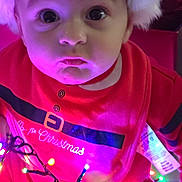Lukas is registered to the contest to win money with this photo: baby, child, christmas, holiday, lights, red_clothing, santa_hat, festive, cute, portrait, indoors, glowing_lights, bib, expression, face, wide_eyes, close_up, celebration, seasonal, winter