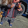 toddler, child, smile, happy, standing, jacket, fuzzy_jacket, sneakers, blue_shoes, hand, adult_hand, parking_lot, car, tire, wheel, asphalt, outdoor, long_hair, winter_clothing, portrait