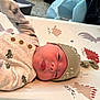 newborn, baby, infant, hat, clothing, dinosaur_pattern, mattress, cute, lying_down, tongue_out, soft_light, indoors, bedroom, knitted_hat, onesie, sleepwear, child, small, adorable, portrait