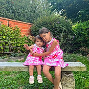 Olivia a rejoint le concours — aidez-le/la à gagner de superbes lots ! child, children, sisters, girl, toddler, matching_dresses, pink_dress, bench, garden, greenery, brick_wall, plants, flowers, outdoor, grass, shoes, embrace, cute, portrait, summer