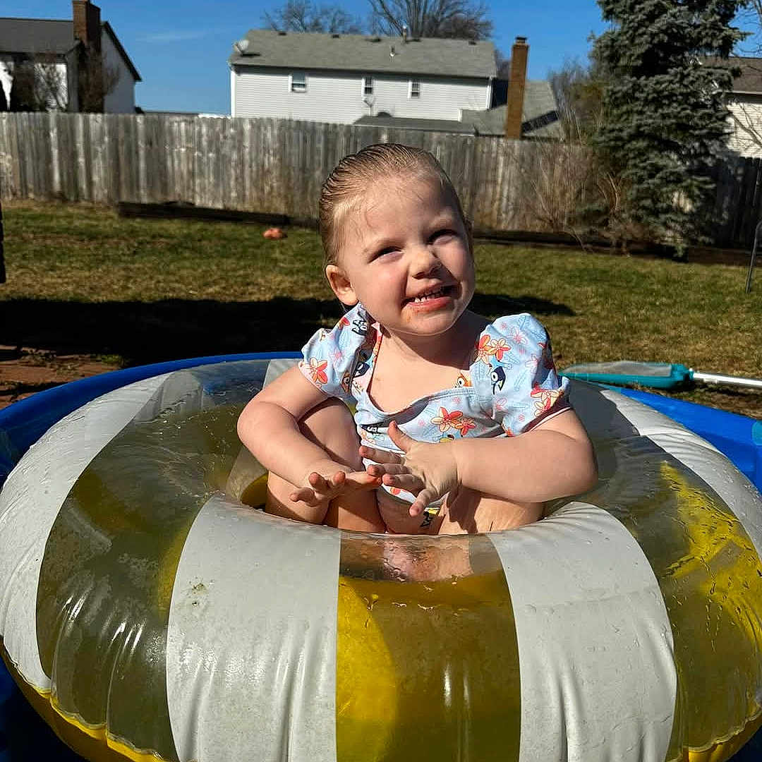 Oakley is registered to the contest to win money with this photo: backyard, child, clothing, daytime, fence, fun, grass, happy, house, inflatable_ring, outdoor, person, play, pool, smiling, summer, sunny, toddler, tree, water