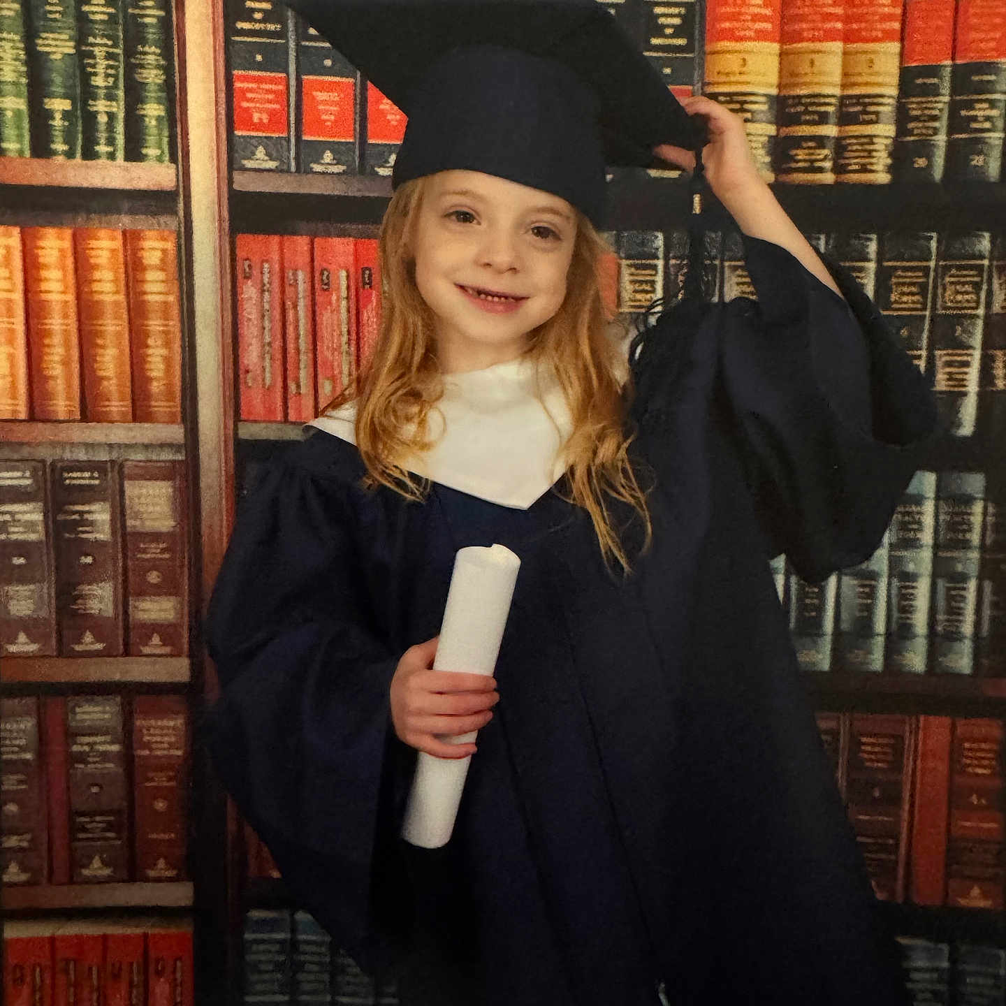 Braelynn is registered to the contest to win money with this photo: academic, achievement, bookshelf, cap, celebration, child, childhood, diploma, education, formalwear, gown, graduation, happy, indoors, library, person, portrait, posing, smile, young