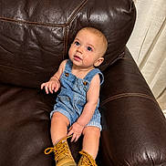 Darell is registered to the contest to win money with this photo: baby, child, infant, sitting, armchair, leather, brown, denim, overalls, boots, golden_shoes, blue_eyes, smiling, portrait, indoor, curtains, furniture, cozy, fashion, photography