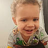 toddler, child, smiling, curly_hair, indoor, bed, blanket, cartoon_clothing, happy, person, portrait, playful, young_child, face, jewelry, gold_chain, curtain, wall, home, casual