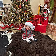 Lainey is registered to the contest to win money with this photo: baby, child, christmas_tree, santa_hat, holiday, presents, gift_wrapping, rug, plush, rocking_horse, stockings, fireplace, decorations, indoor, festive, toddler, cute, smiling, cozy, holiday_season