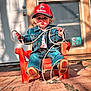 child, denim_jacket, red_cap, lasso, plastic_chair, outdoor, backyard, pavement, door, window, sunlight, cowboy, jeans, footwear, playful, posing, young_child, hat, rope, expression