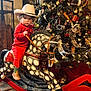 Lainey is registered to the contest to win money with this photo: child, toddler, cowboy_hat, rocking_horse, christmas_tree, holiday_decor, boots, red_clothing, indoor, festive, decorations, toy, wooden_floor, lights, pine_tree, wrapped_gifts, fur_rug, curly_hair, face, portrait