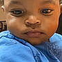 Kelvin joined the competition — help win amazing prizes! child, toddler, face, portrait, blue_shirt, curly_hair, indoor, close_up, baby, expression, person, young_child, casual_clothing, skin, head, human, eyes, sleeve, background, video_call