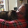 affection, casual_clothing, cat, comfort, cozy, cuddling, domestic, door, flowers, furniture, home, indoor, love, pantry, person, plaid_shirt, relaxing, seated, tabby_cat, wall_decoration
