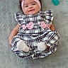 baby, infant, smile, headband, pink, plaid, dress, bow, pacifier, lying, soft_surface, cute, child, happy, indoors, person, footwear, sock, texture, fabric
