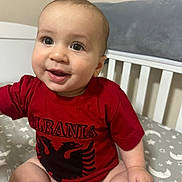 Enzo joined the competition — help win amazing prizes! baby, child, smiling, red_shirt, crib, diaper, indoor, happy, face, person, infant, sitting, cute, drool, cushion, blanket, pattern, head, skin, clothing