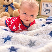 Mateo is registered to the contest to win money with this photo: baby, blanket, blue_eyes, child, close_up, cozy, framed_sign, garden, happy, infant, lying_down, nursery, outdoor, portrait, red_shirt, smiling, soft_lighting, star_pattern, stuffed_animal, teddy_bear