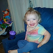 Stormie joined the competition — help win amazing prizes! toddler, child, smiling, sitting, armchair, blue_clothing, tie_dye_shirt, barefoot, toy, sippy_cup, indoor, curtains, carpet, happy, face, person, hair, playful, colorful, home