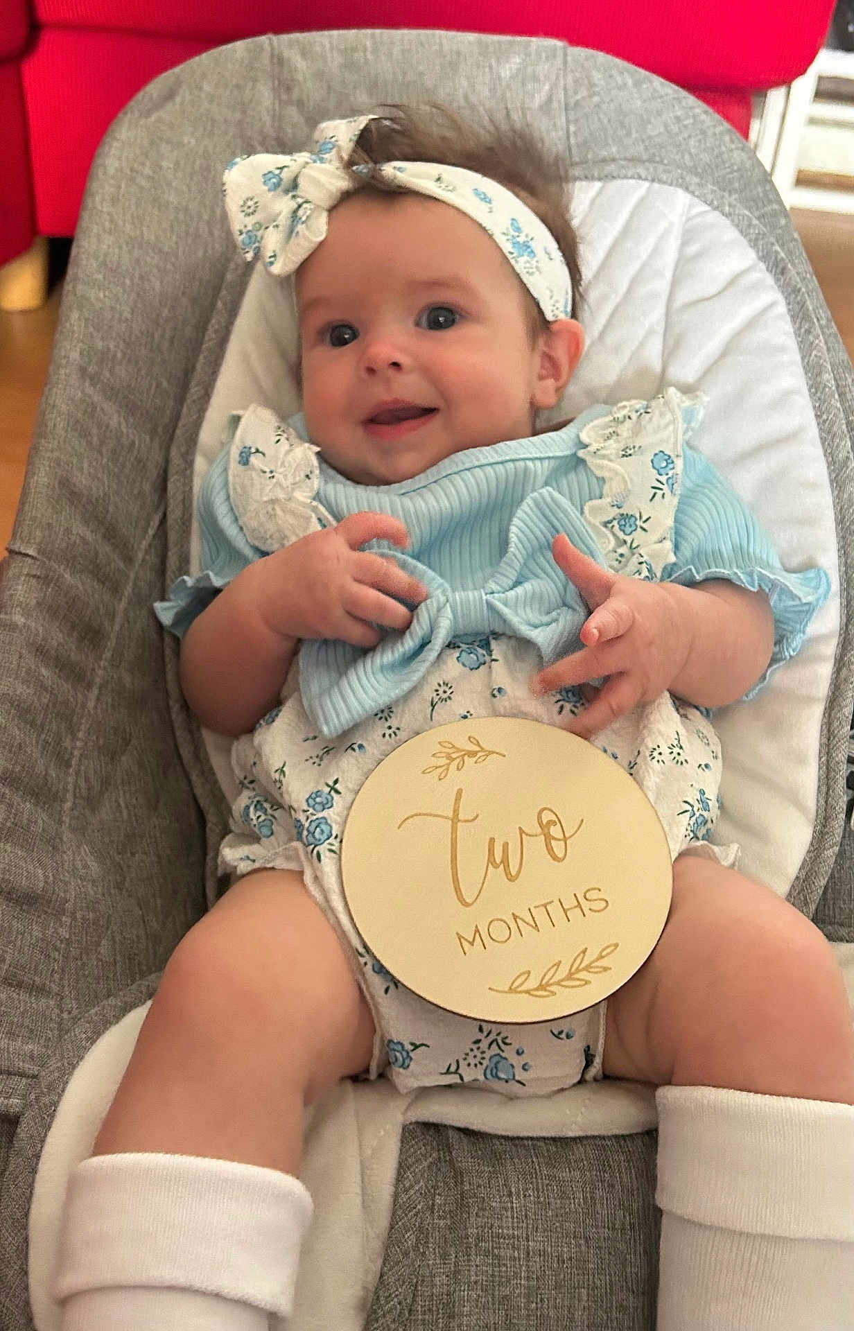 Hallie is registered to the contest to win money with this photo: baby, infant, smiling, headband, blue_clothing, milestone_sign, two_months, baby_seat, cushion, happy, cute, portrait, indoor, child, person, skin, legs, hands, socks, fabric