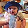 Lux is registered to the contest to win money with this photo: baby, child, hat, bucket_hat, striped_clothing, kitchen, countertop, hands, person, indoor, curious, blue_eyes, infant, cute, chubby, face, holding, natural_light, domestic, young