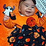 baby, smiling, halloween, pumpkin, bat, orange_clothing, headband, blanket, cartoon_ghost, cute, festive, infant, happy, costume, black_skirt, patterned_clothing, baby_girl, lying_down, indoor, celebration