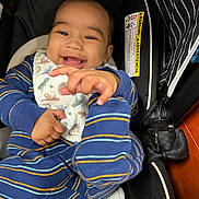 Sterling is registered to the contest to win money with this photo: baby, infant, smile, car_seat, bib, striped_pajamas, hand, reaching, happy, teeth, warning_label, fabric, close_up, portrait, stroller, cozy, blue, cute, seat_belt, playful
