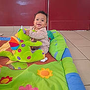 Hayden a rejoint le concours — aidez-le/la à gagner de superbes lots ! baby, child, clothing, colorful, cute, dragon, floor, green, happy, indoor, person, play_mat, plush_toy, portrait, red, sitting, smiling, tile, toy, wall