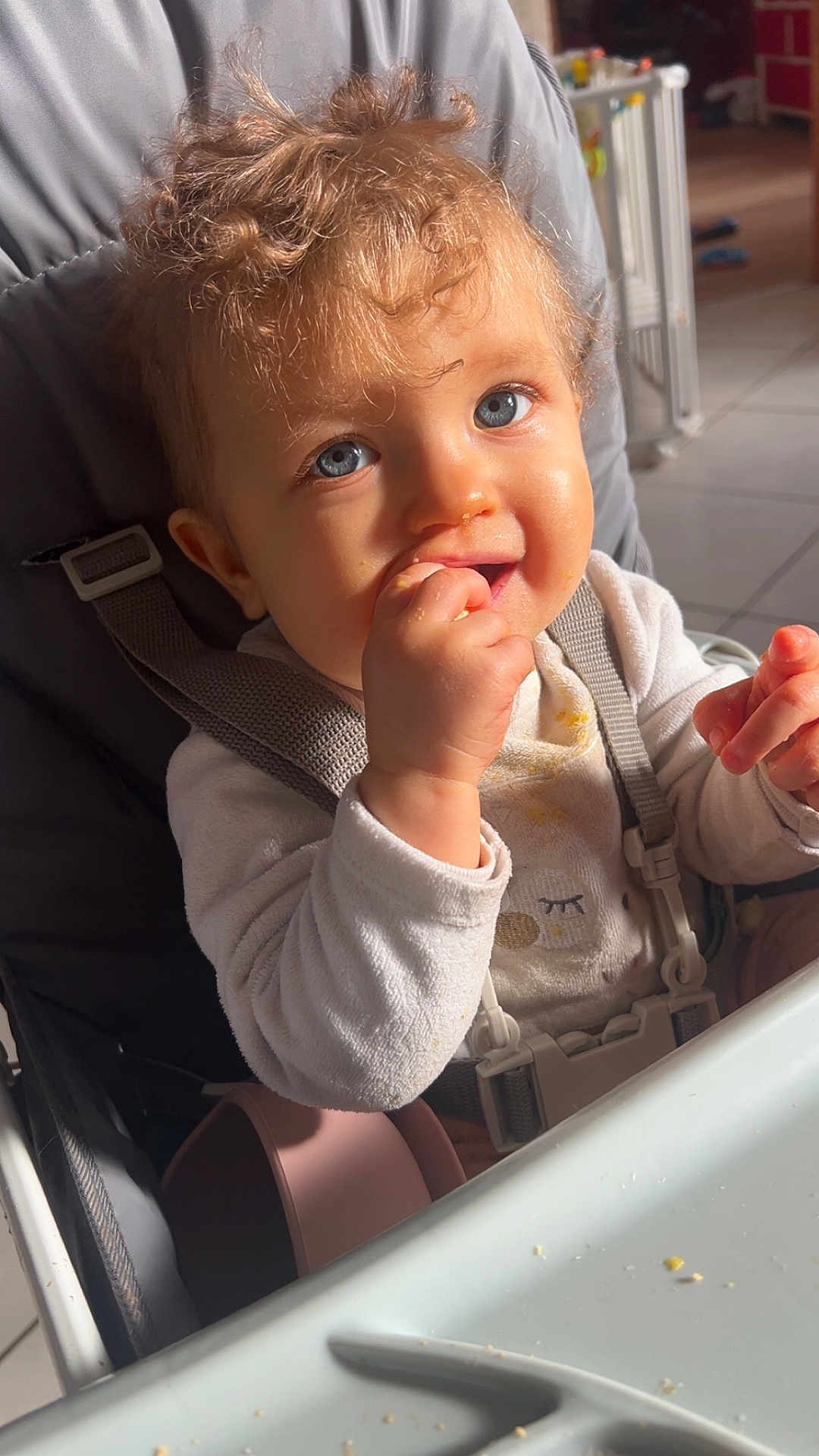 Kaïssy a rejoint le concours — aidez-le/la à gagner de superbes lots ! baby, child, high_chair, curly_hair, blue_eyes, messy, snack_time, feeding, indoor, toddler, white_clothing, happy, cute, person, seatbelt, table, food_crumbs, natural_light, kitchen, smiling